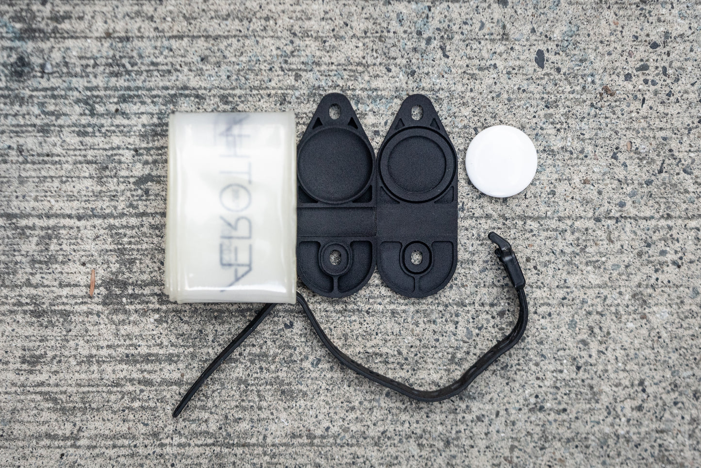 Image: The Standby Tube Strap Bracket, a clever bike accessory that conceals an Apple AirTag within a discreet bracket used to carry a spare tube on your bike. This lightweight and durable bracket is designed to blend in seamlessly and does not resemble a typical AirTag holder. It is specifically designed for use with Aerothan and Tubolito tubes and comes complete with a Voile Nano strap for easy installation. Made in Canada. top down open.