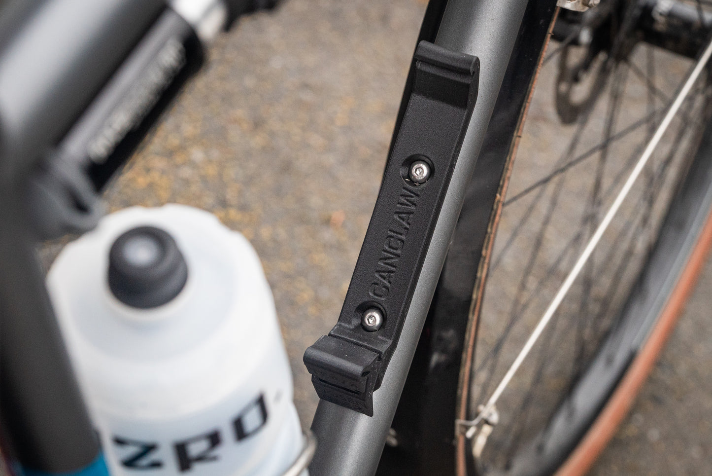 Image: The Canclaw, a lightweight and low-profile bike drink holder designed for standard 12oz (355ml) cans and 16oz (473ml) tall cans. It securely grips your beverage and can be attached using standard bottle cage bolt spacing or zipties. This product is 3D printed to order from ultra-strong carbon fiber nylon material and proudly made in Canada. Top down.