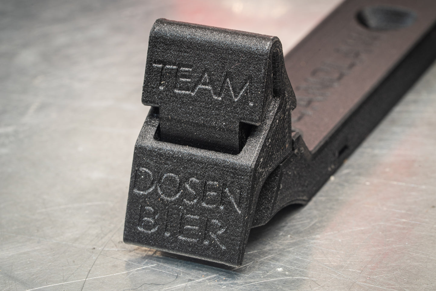 Image: The Canclaw, a lightweight and low-profile bike drink holder designed for standard 12oz (355ml) cans and 16oz (473ml) tall cans. It securely grips your beverage and can be attached using standard bottle cage bolt spacing or zipties. This product is 3D printed to order from ultra-strong carbon fiber nylon material and proudly made in Canada. Text Closeup.